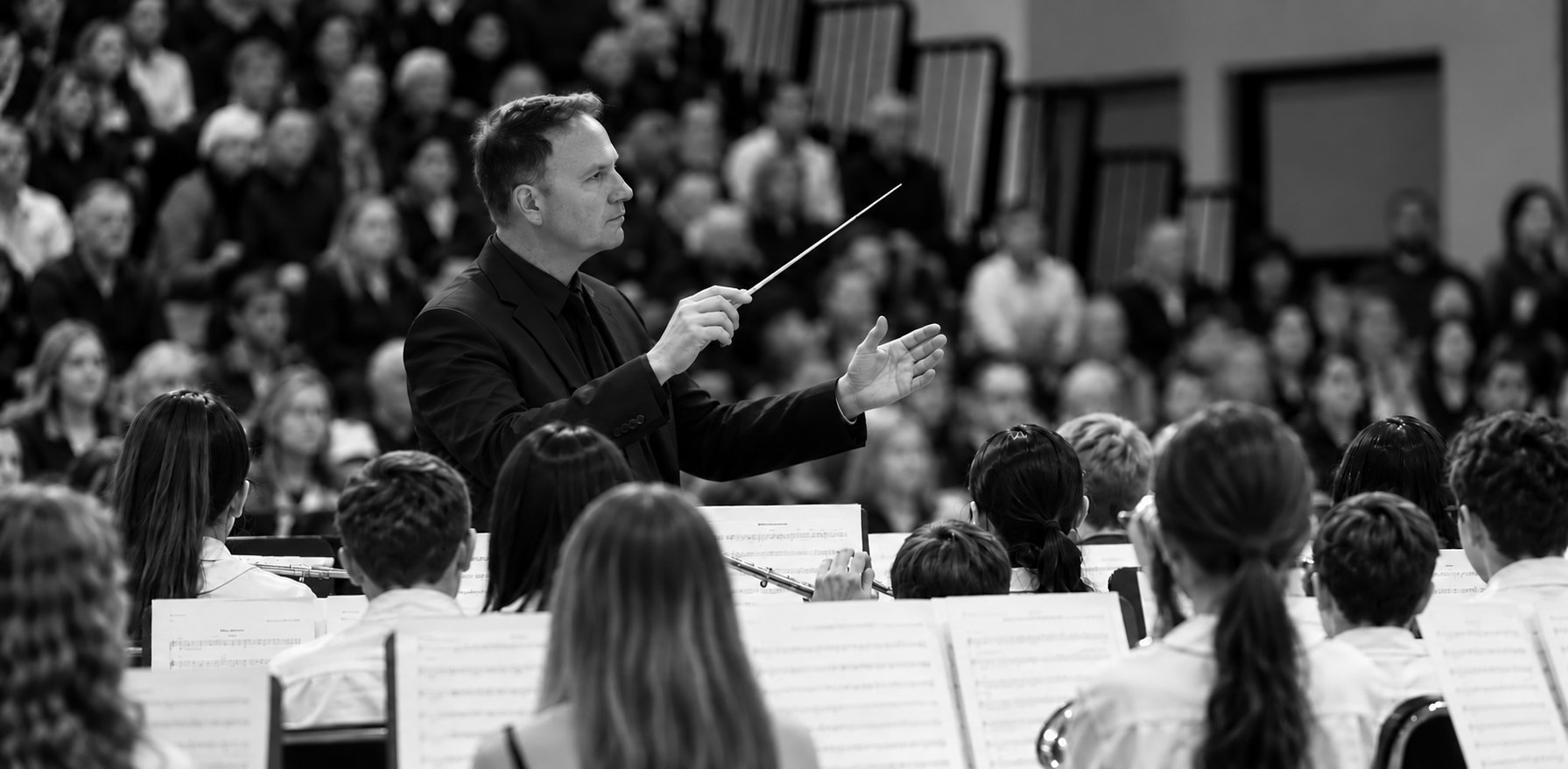 Rob Hutchinson conducting a school band, baton raised, with the audience behind