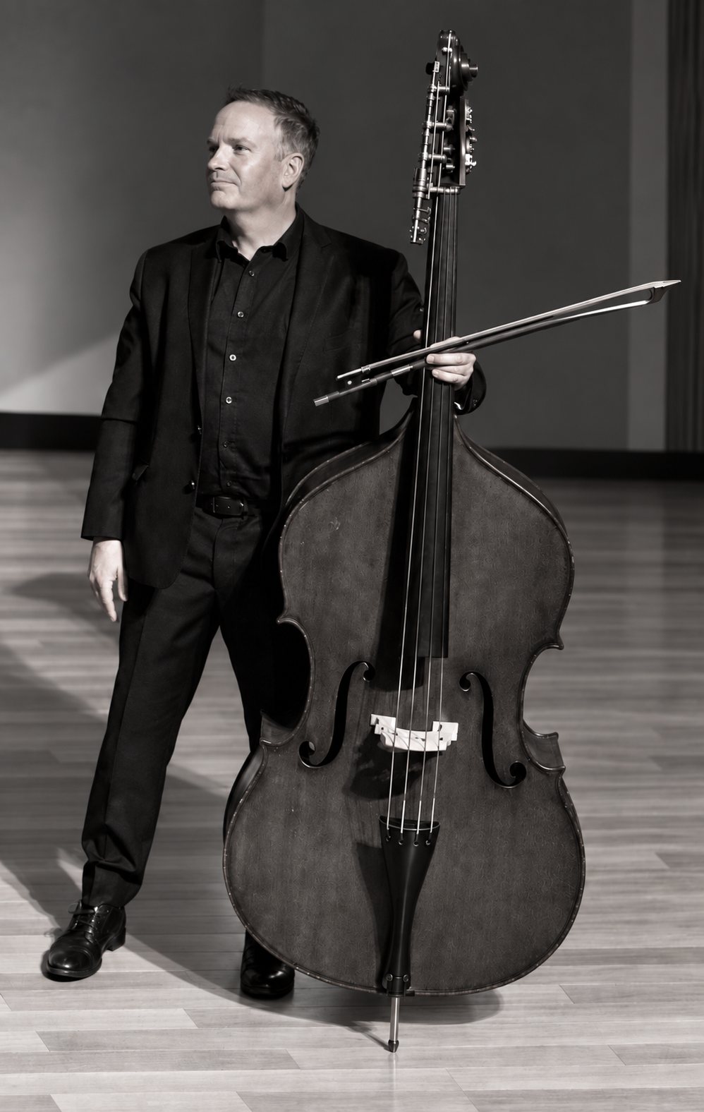 Rob Hutchinson standing beside his double bass, holding the bow